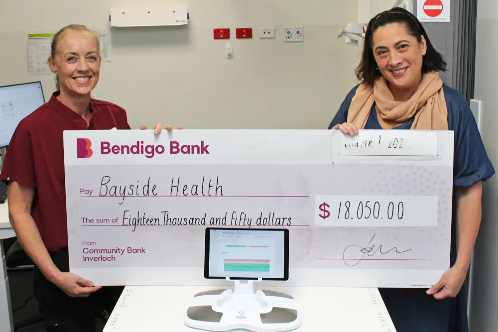 Bayside Health Regional Lymphoedema Practitioner Michelle McMahon and Fundraising and Volunteer Manager Kerry Redmond hold the cheque in front of the Sozo Machine.